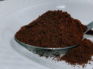 Closeup aromatic organic ground coffee heaped in silver teaspoon on white ceramic plate on table in cafeteria kitchen